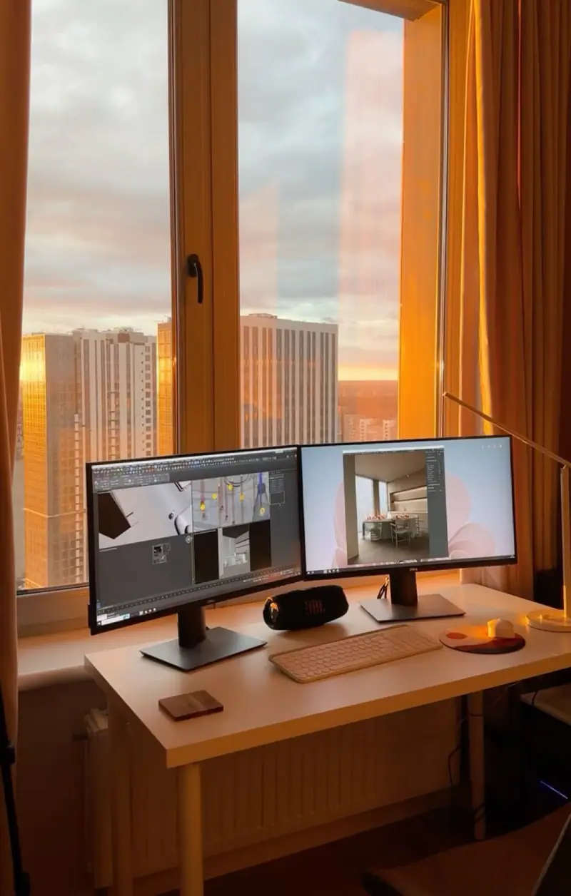 Escritorio con dos monitores frente a una ventana al atardecer